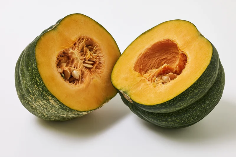 Two halves of a kabocha squash cut open showing orange flesh and seeds on white background