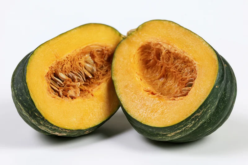 Two halves of a kabocha squash cut open showing seeds and orange flesh on white background