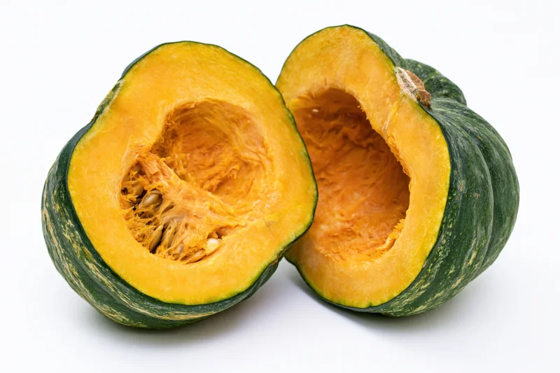Two halves of a kabocha squash cut open showing orange flesh and seeds on white background