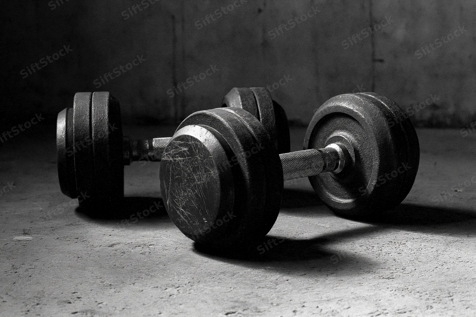 Two iron dumbbells resting on a rough concrete gym floor