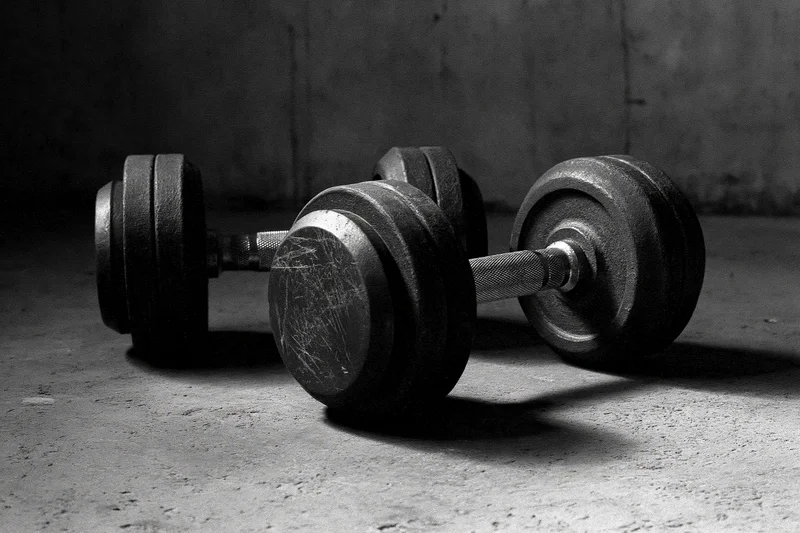 Two iron dumbbells resting on a rough concrete gym floor