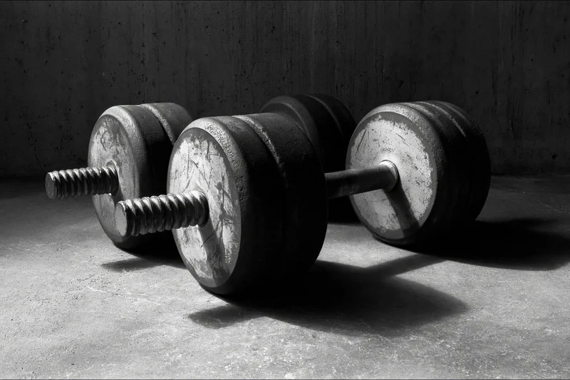 Two iron dumbbells resting on a rough concrete gym floor