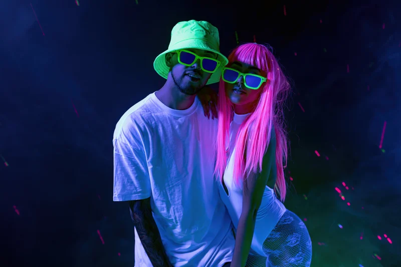 Couple posing together under uv blacklight in a nightclub with neon glow and confetti