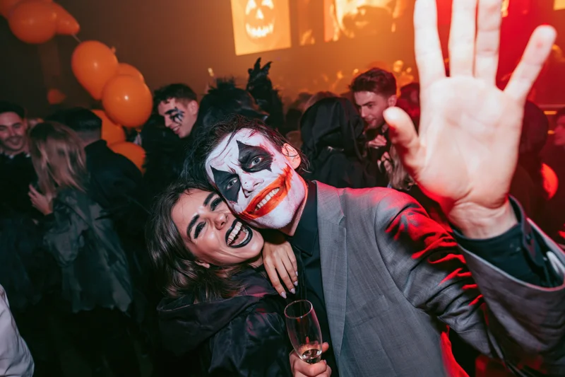 Couple in halloween costumes dancing at a nightclub with orange balloons and pumpkin lights