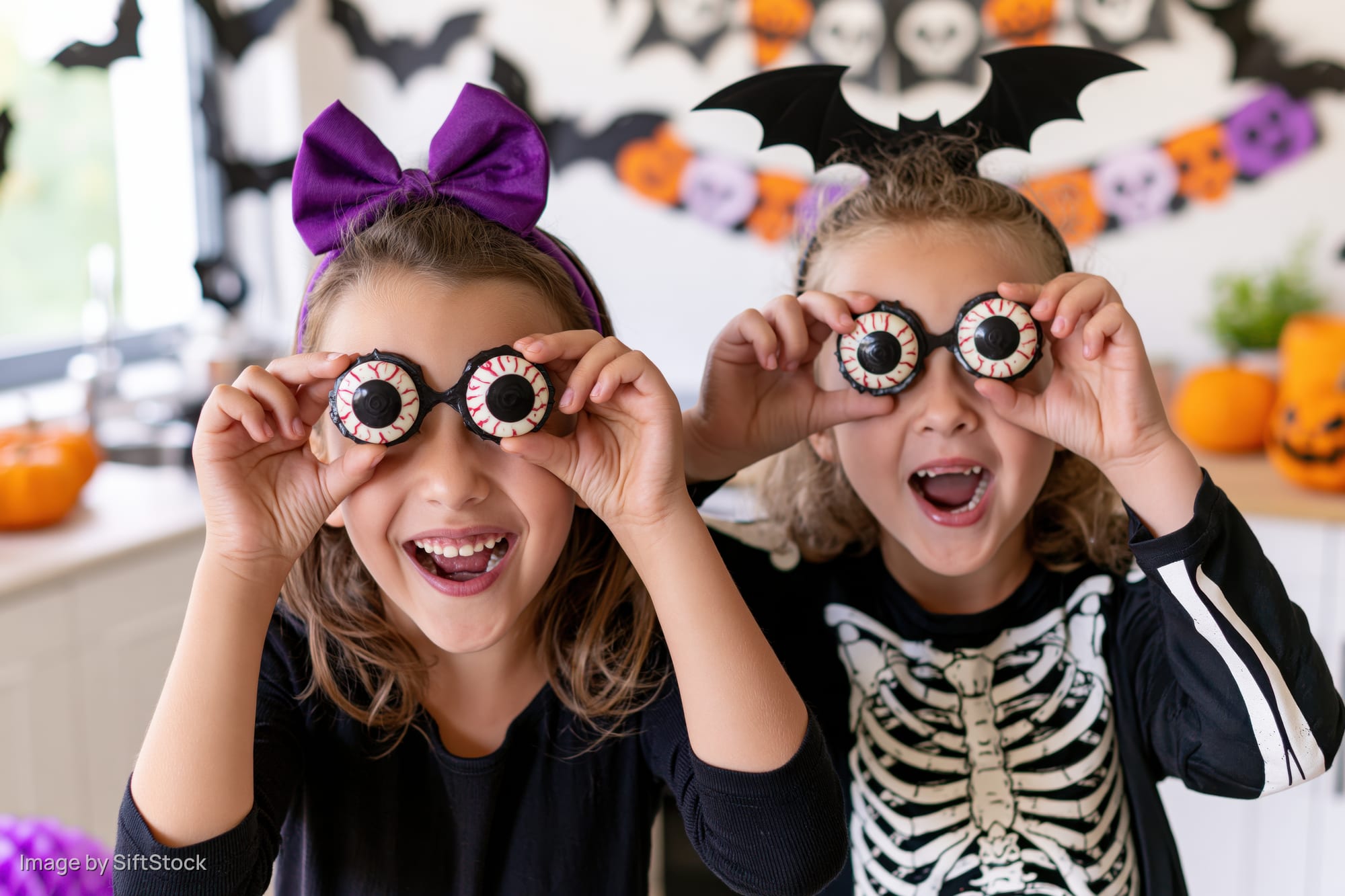 Two young girls laughing while holding plastic eyeball candies at a halloween party in a kitchen