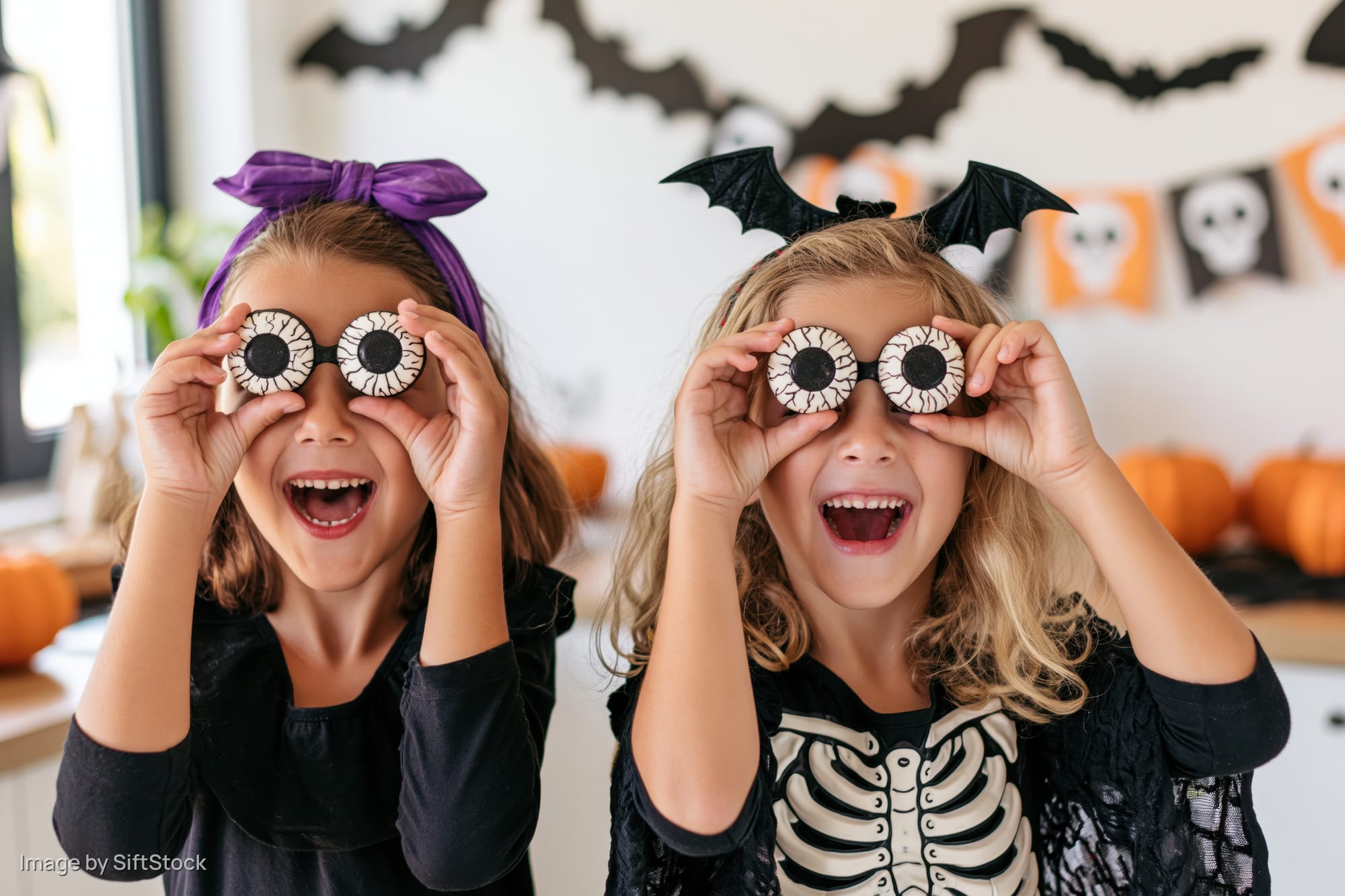 Two young girls laughing while holding plastic eyeball candies at a halloween party in a decorated home