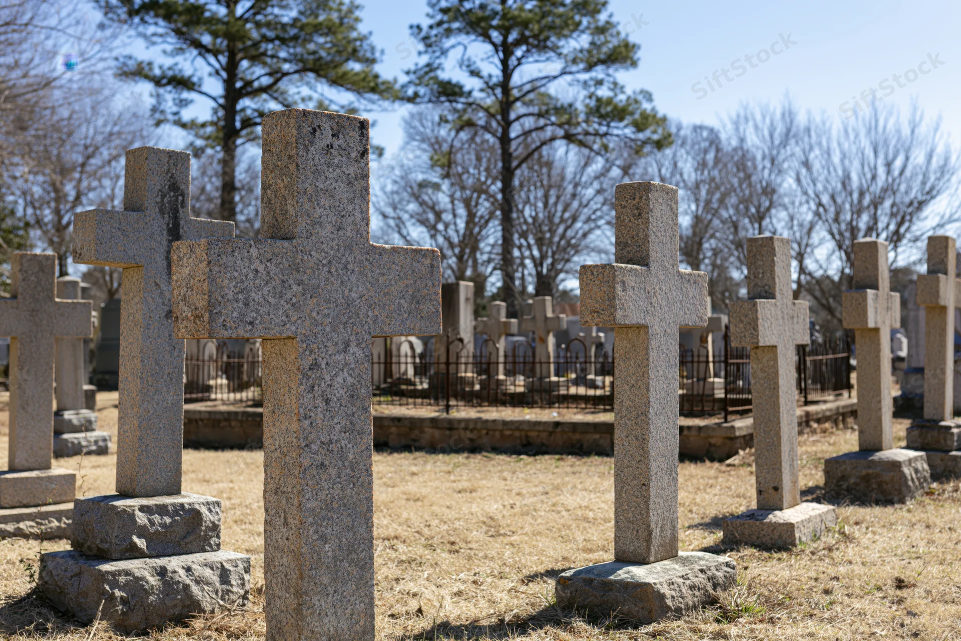 Rows of weathered granite cross grave markers in a cemetery under a clear sky