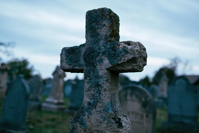 Weathered stone cross gravestone in an old cemetery at dusk