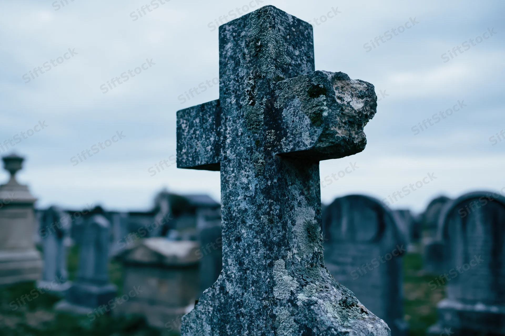 Weathered stone cross gravestone in an old cemetery with blurred tombs in the background