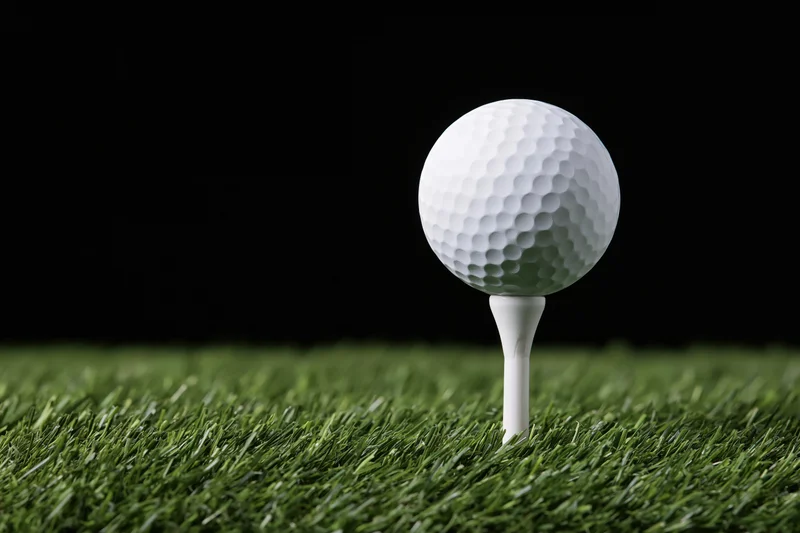 White golf ball on a white plastic tee set in green grass against black background