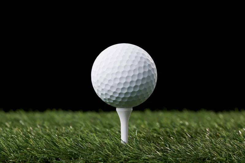 White golf ball on a white plastic tee resting on green grass against black background