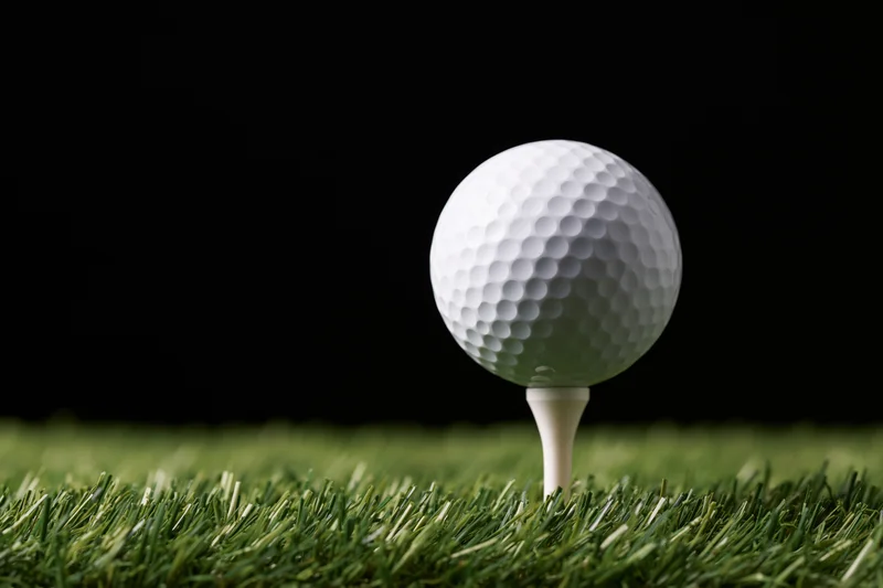 White golf ball on a tee set in green grass against black background