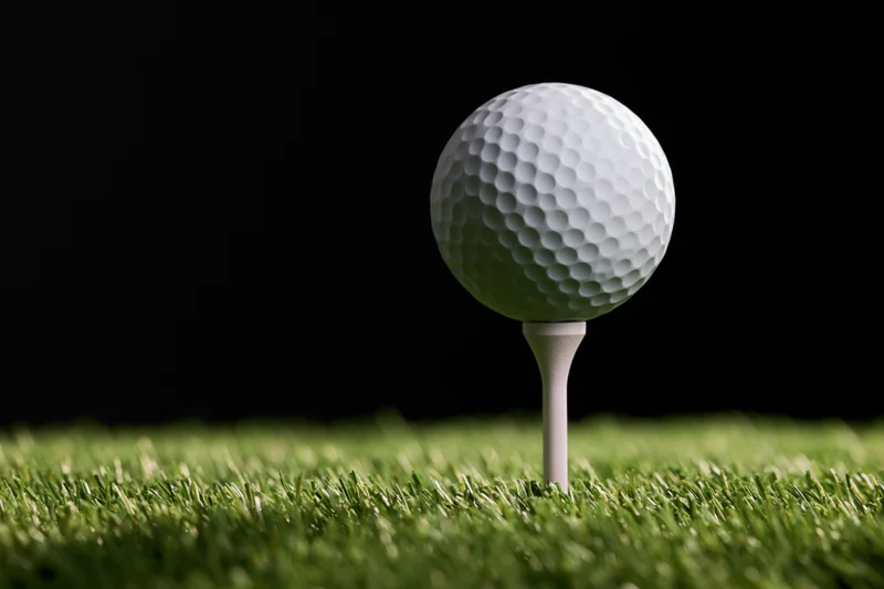 White golf ball on a plastic tee set in green grass against black background