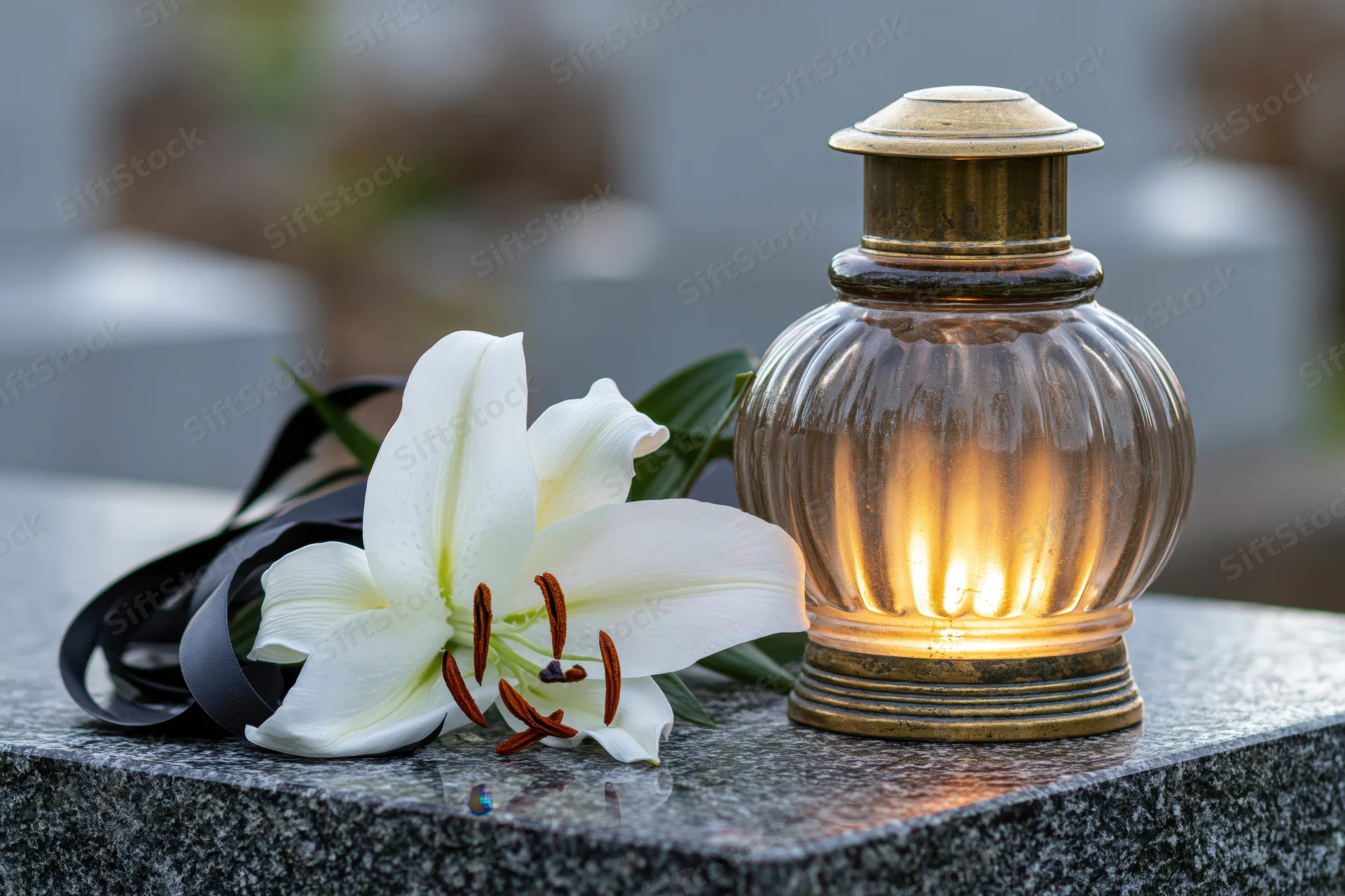 White lily with black ribbon and lit candle on granite tombstone