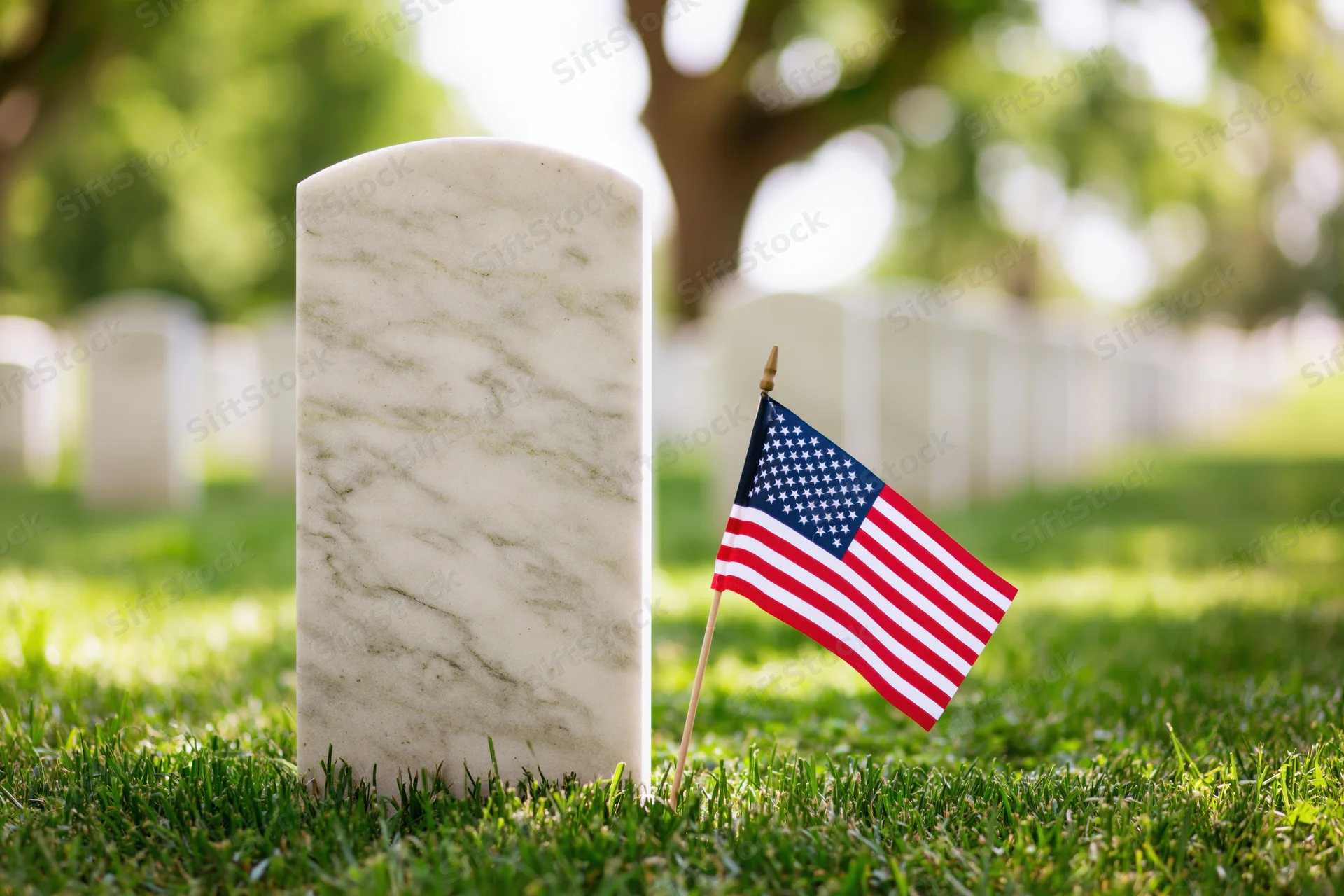 White marble military headstone in a cemetery with a small american flag planted beside it on green grass