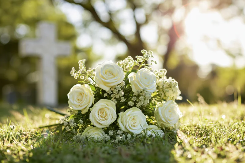 White rose bouquet resting on green cemetery grass near a cross