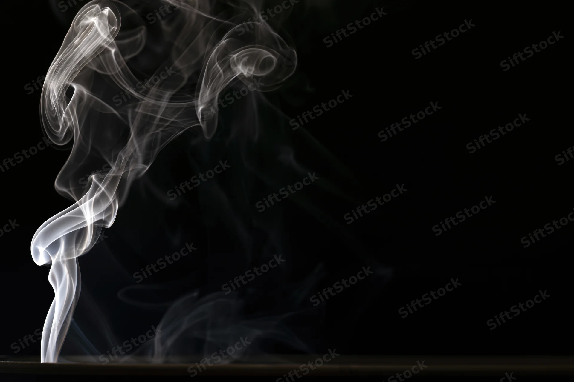 White smoke curling upward in delicate swirls against a black background