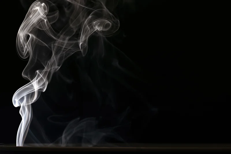 White smoke curling upward in delicate swirls against a black background