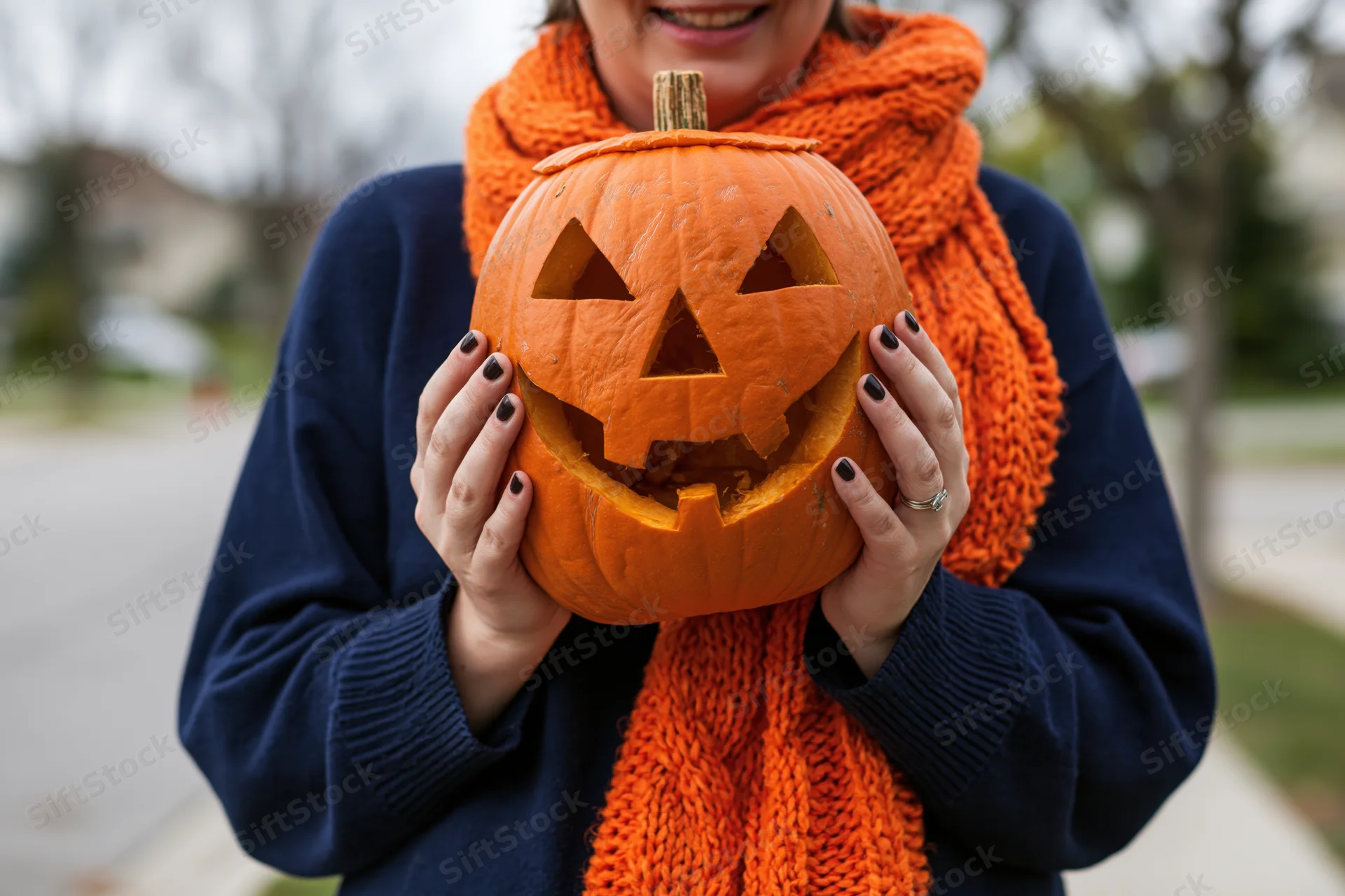 Woman holding carved jack-o-lantern outdoors on sidewalk