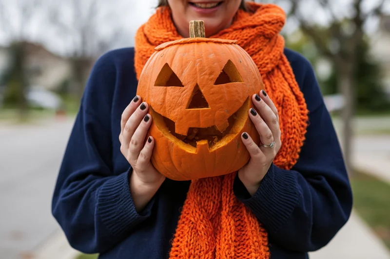 Woman holding carved jack-o-lantern outdoors on sidewalk