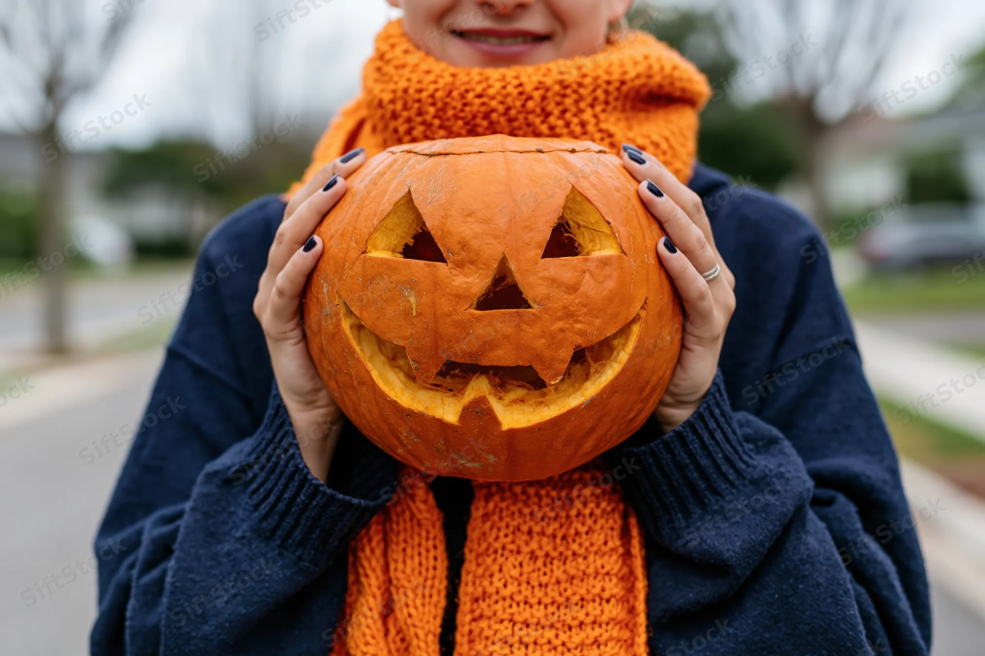 Woman holding carved jack-o-lantern in front of her face outdoors on a sidewalk