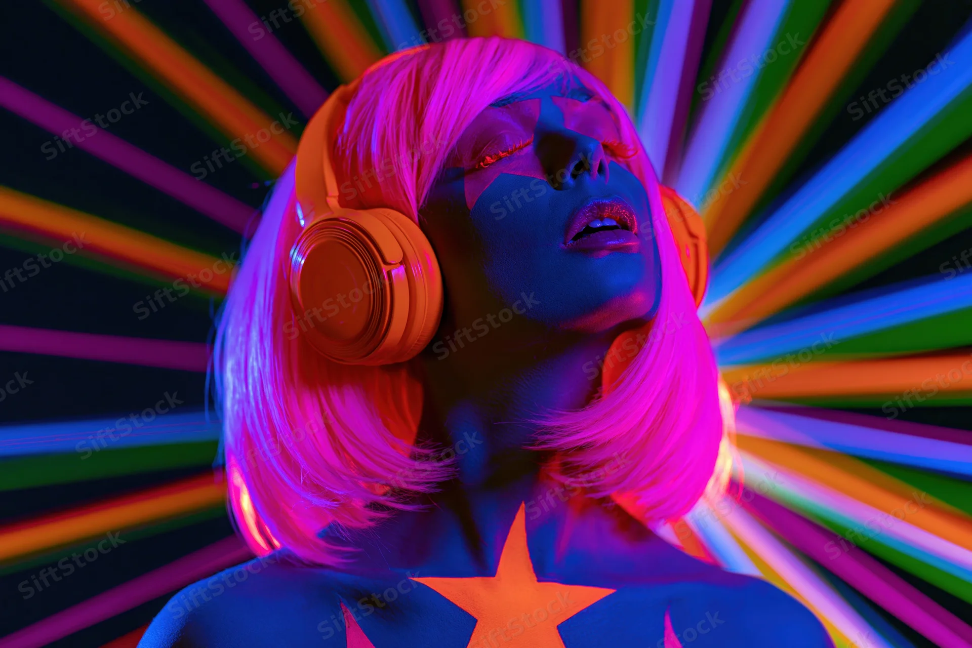 Woman with glowing uv body paint and orange headphones against rainbow light burst