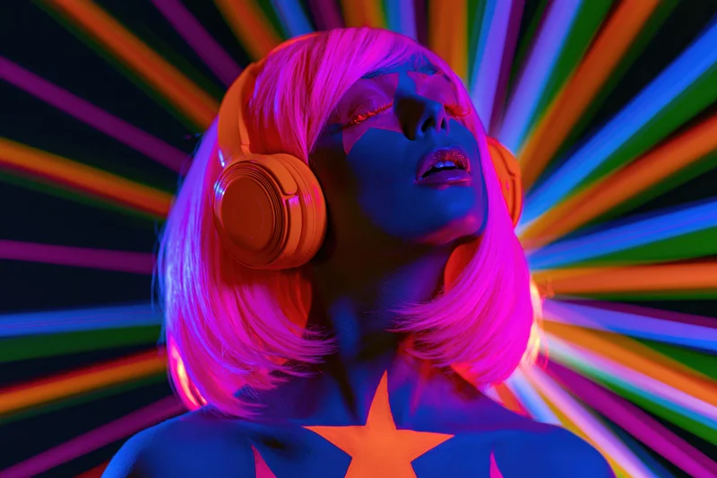 Woman with glowing uv body paint and orange headphones against rainbow light burst