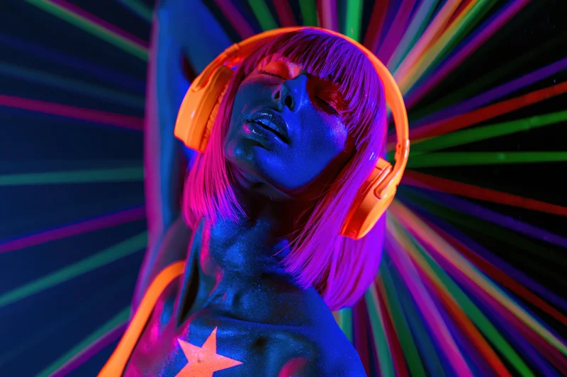 Woman with glowing uv body paint and orange headphones in a colorful neon light environment