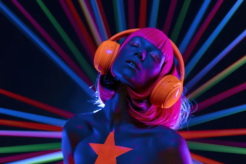 Woman with orange headphones and glowing uv body paint star under neon light rays