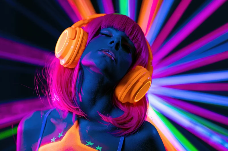 Woman with orange headphones and glowing uv body paint under neon lights