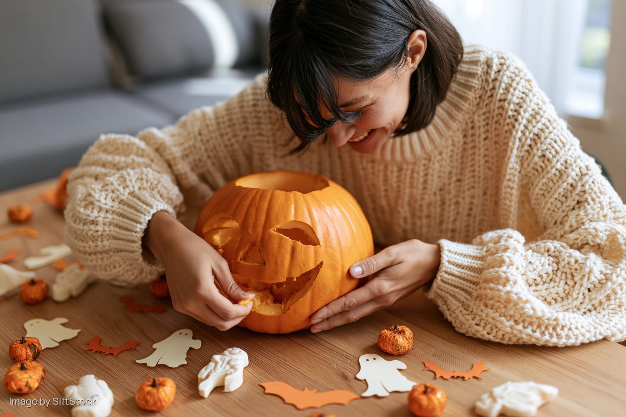 Woman carving a pumpkin on a wooden table surrounded by halloween decorations