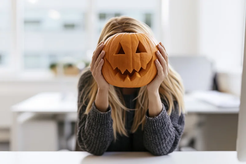 Woman holding carved pumpkin over face at office desk