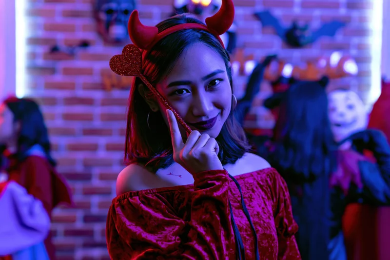 Young asian woman in red devil costume posing with hand near face at halloween party