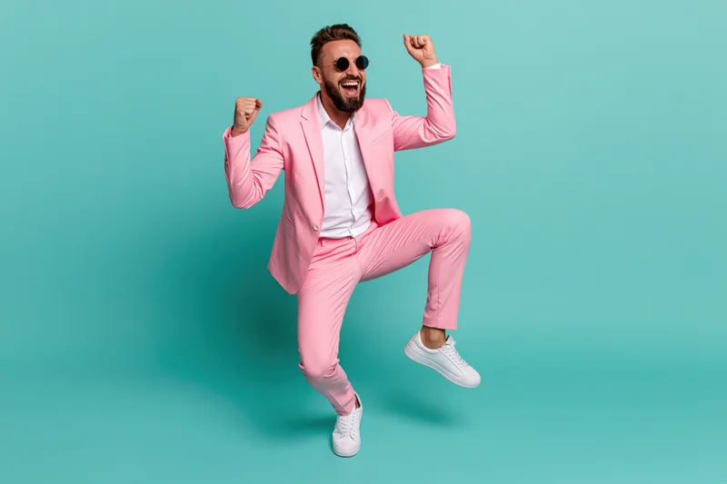 Man in pink suit dancing and celebrating with fists raised against turquoise background