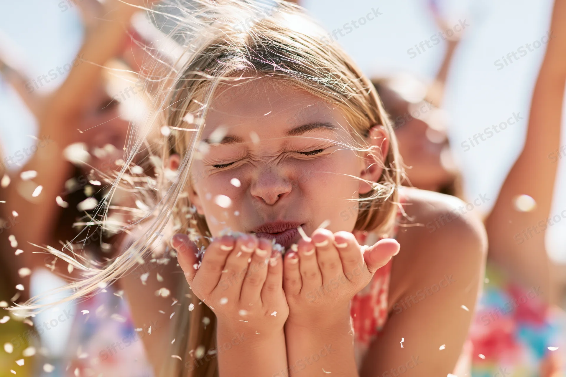 Young blonde woman blowing confetti outdoors at a beach party