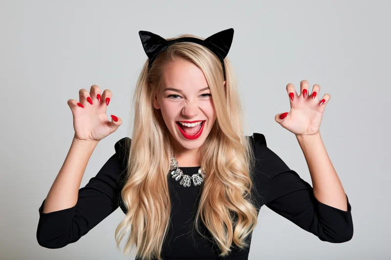 Blonde woman in cat costume smiling with raised hands and claws in studio