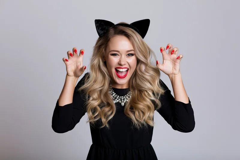 Young blonde woman in halloween cat costume smiling with raised hands in studio