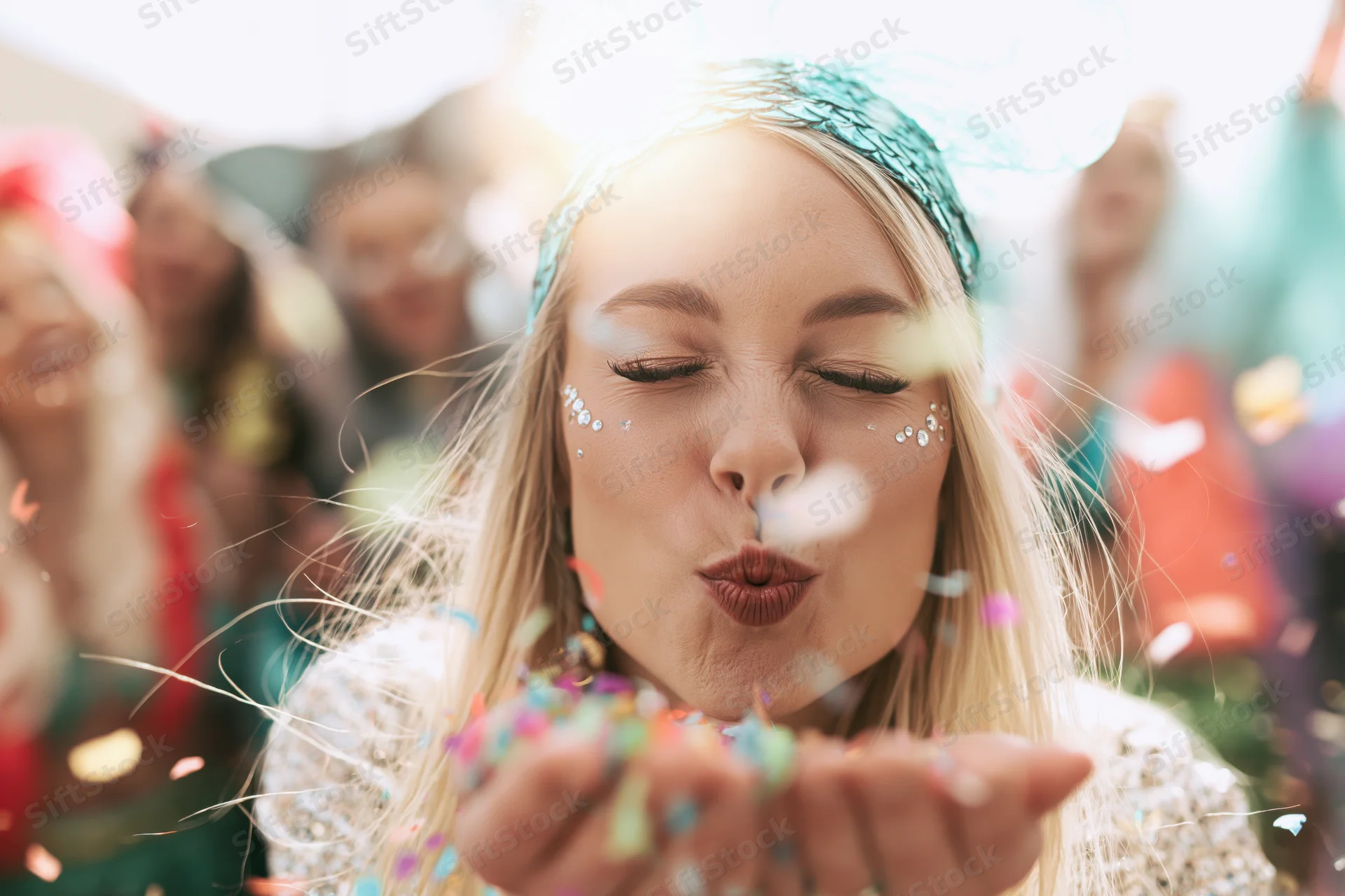 Blonde woman blowing confetti from her hands at a festive outdoor party