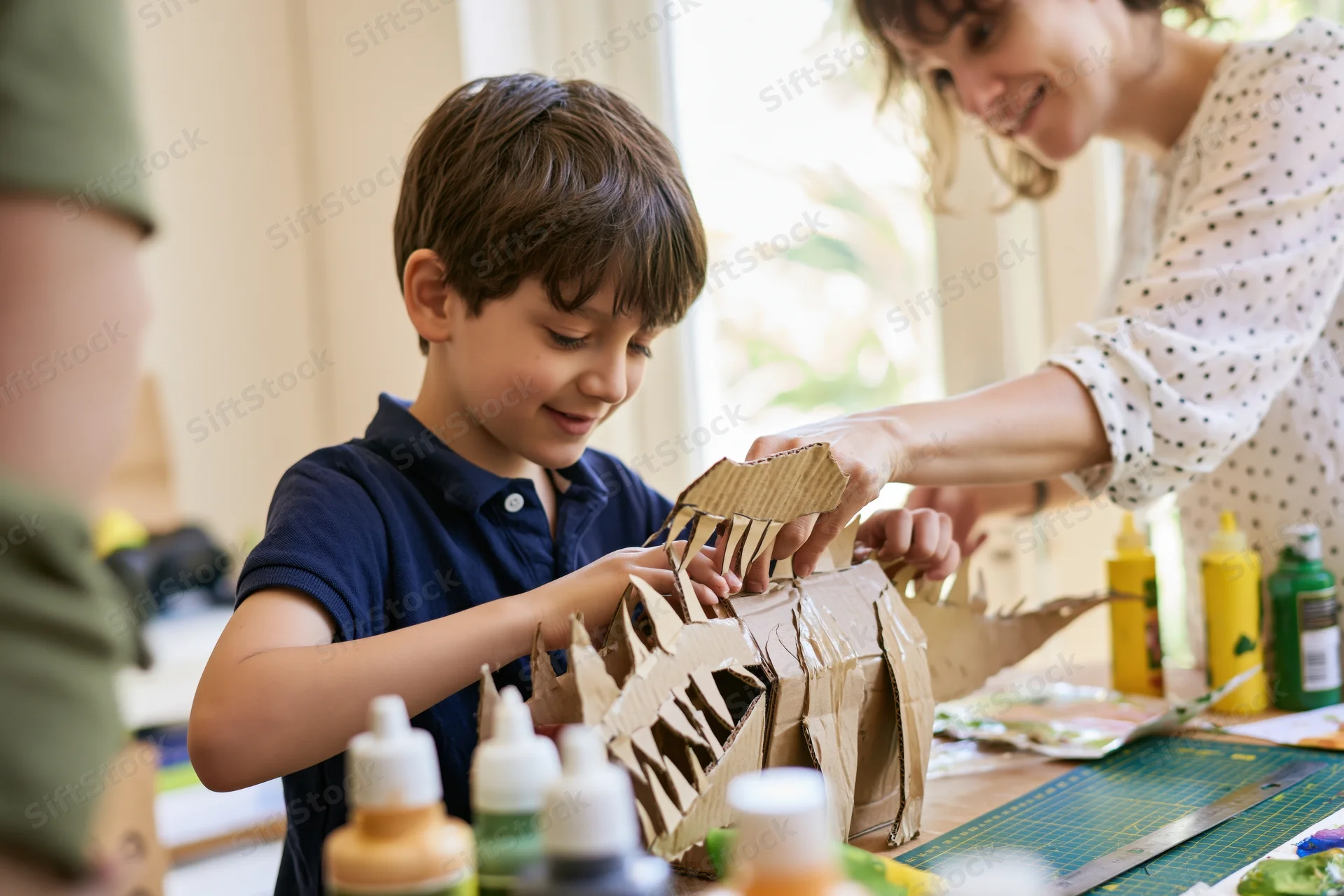 Young boy assembling a cardboard craft with his mother at a table indoors
