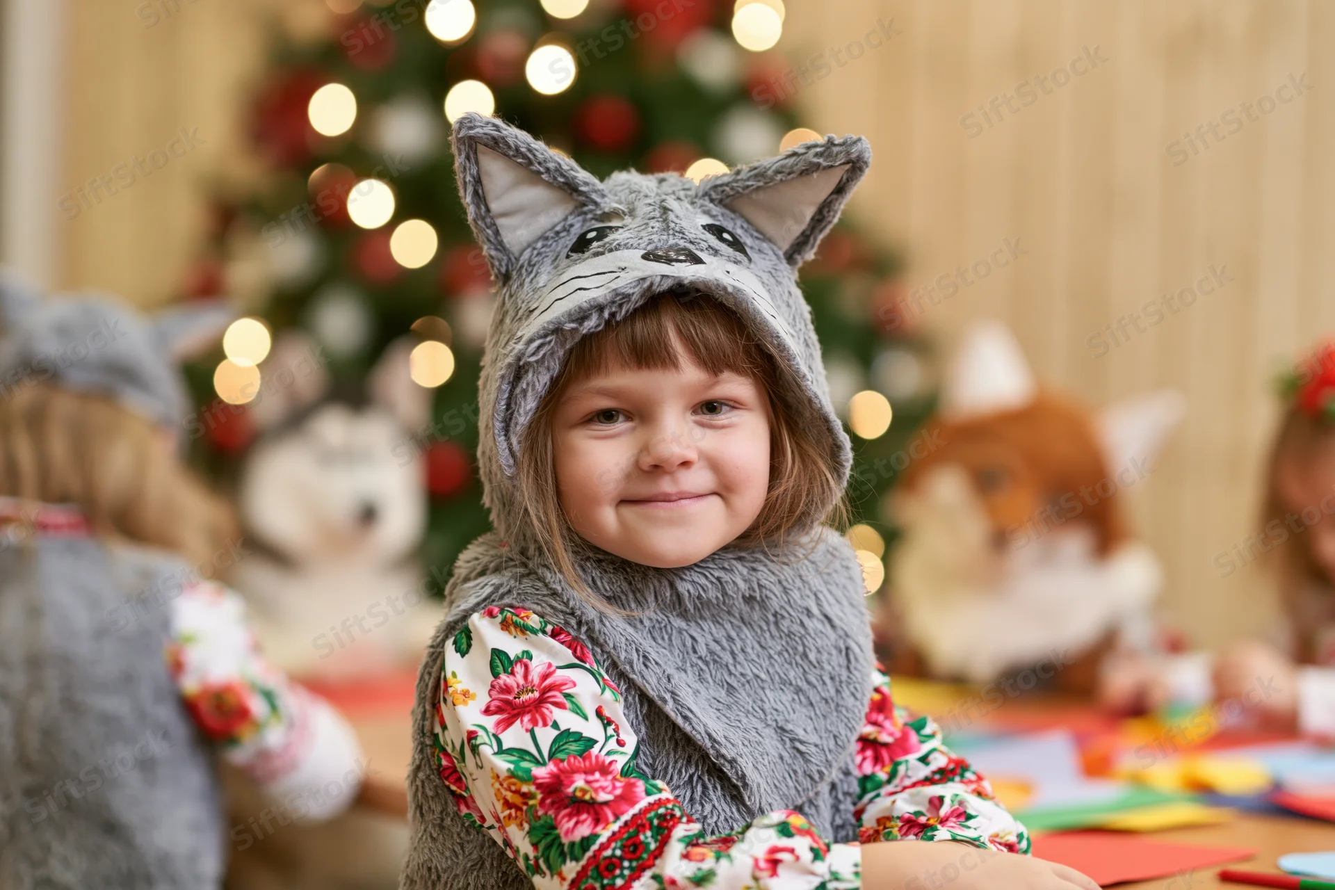 Young girl in grey wolf costume smiling at table with craft supplies during christmas celebration