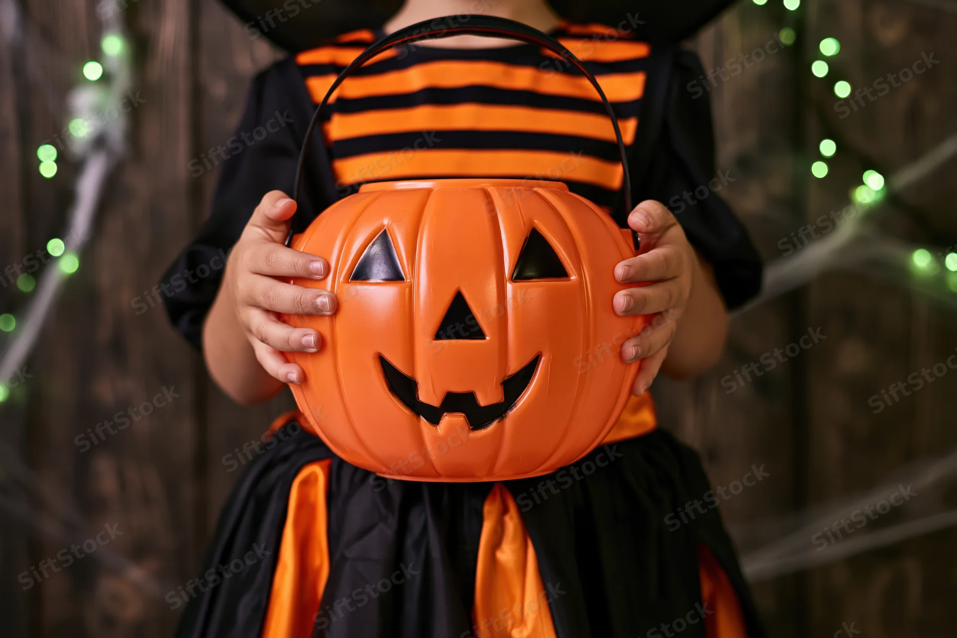 Young girl in witch costume holding orange pumpkin bucket for halloween trick or treat