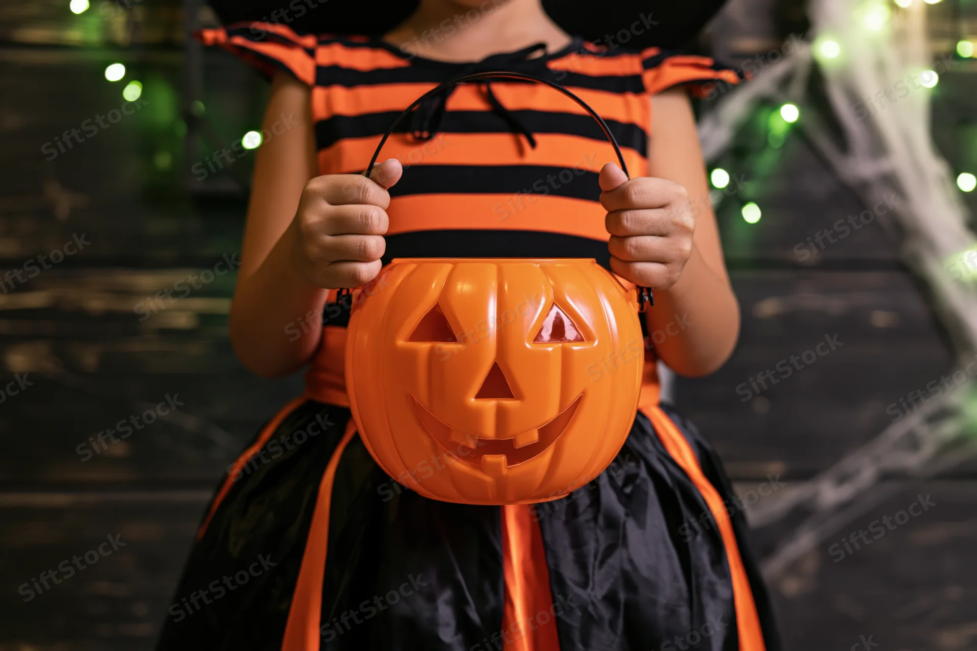 Child in witch costume holding orange pumpkin bucket for halloween trick or treat