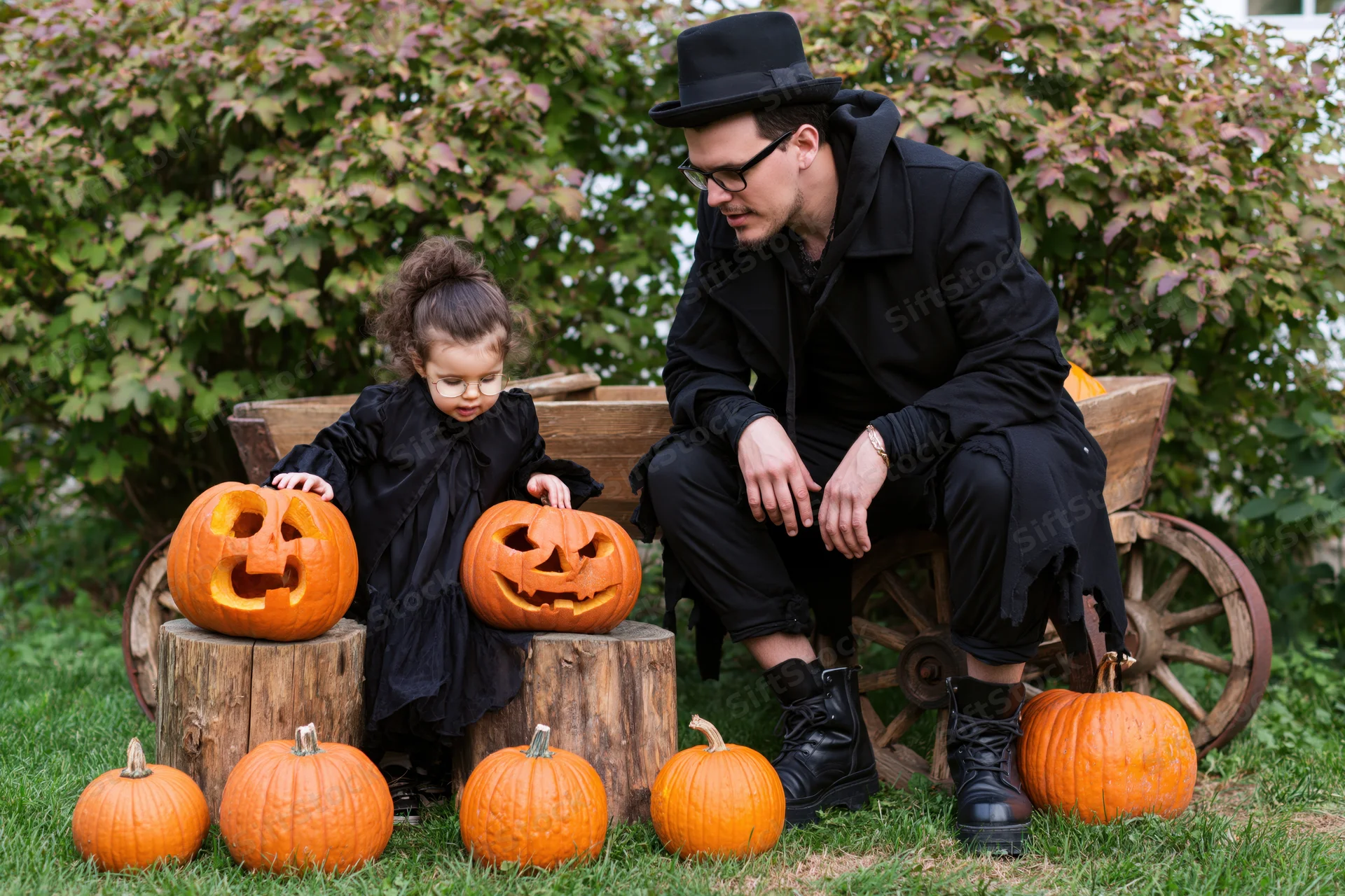 Father and toddler in halloween costumes examining carved pumpkins in a garden