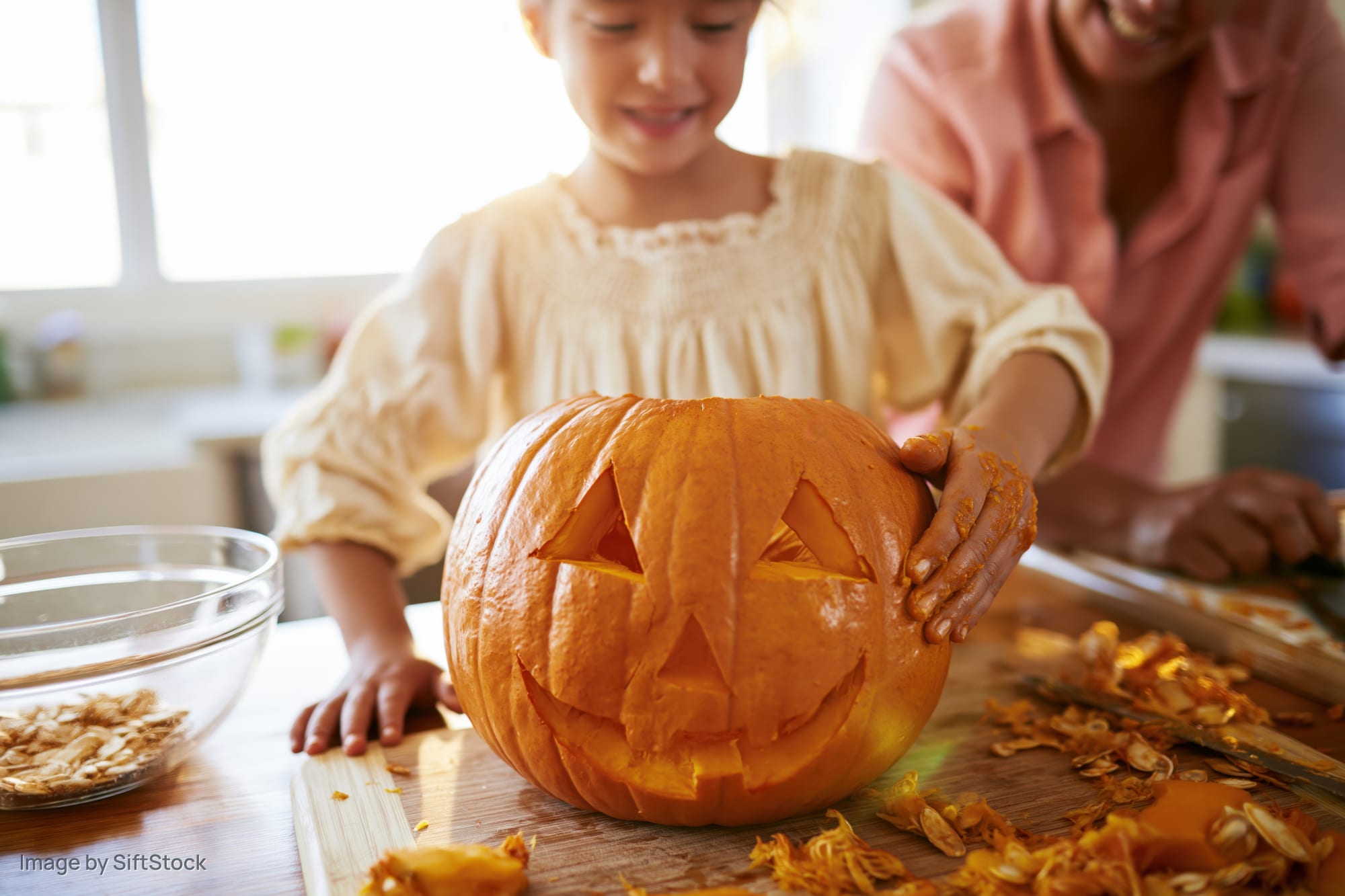 Young girl carving a jack-o-lantern with an adult in a kitchen