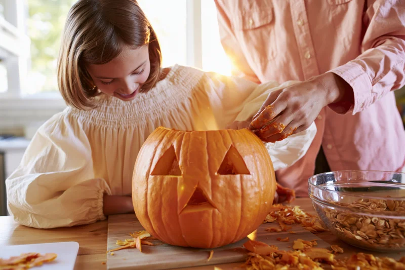Young girl carving a jack-o-lantern with an adult in a kitchen