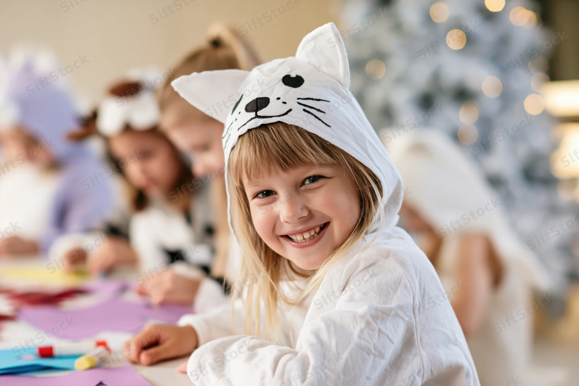 Young girl in white cat costume smiling at camera during holiday craft activity indoors
