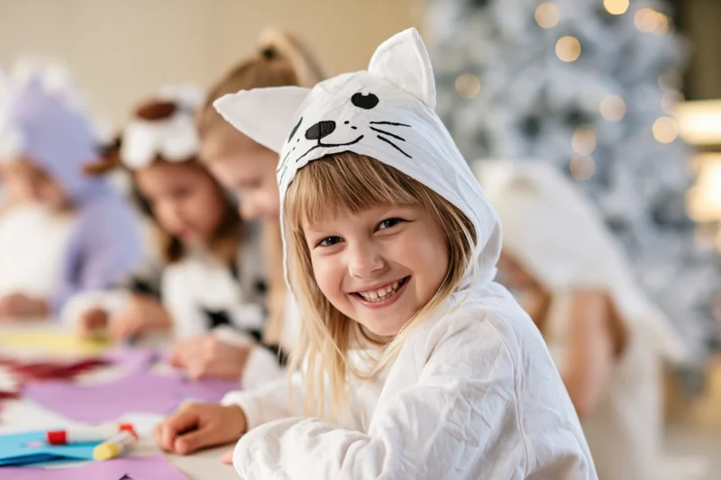 Young girl in white cat costume smiling at camera during holiday craft activity indoors