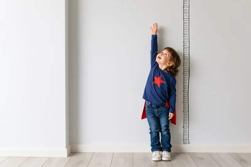 Toddler girl reaching up to measure her height on a wall ruler at home