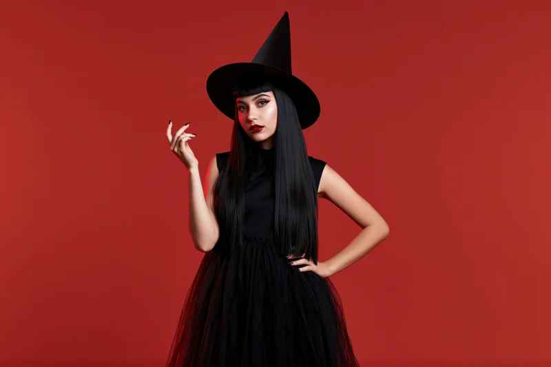 Young woman in witch costume posing with hand on hip against red background