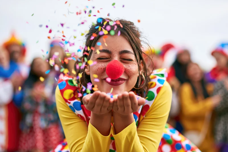Woman in clown costume blowing confetti at outdoor celebration